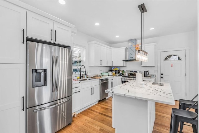 kitchen with hanging light fixtures, white cabinetry, appliances with stainless steel finishes, and wall chimney range hood