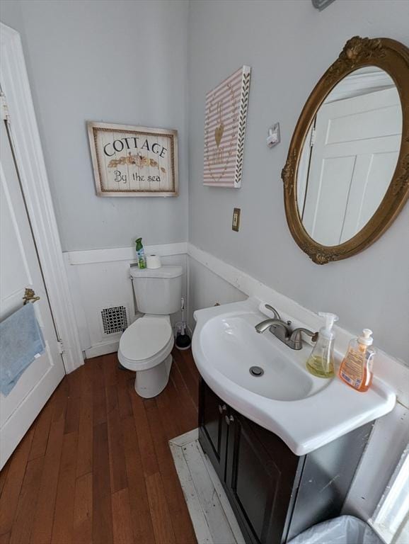 bathroom with hardwood / wood-style flooring, visible vents, a wainscoted wall, toilet, and vanity