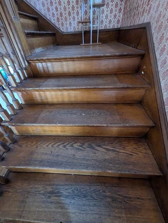 stairs with wallpapered walls and wood finished floors