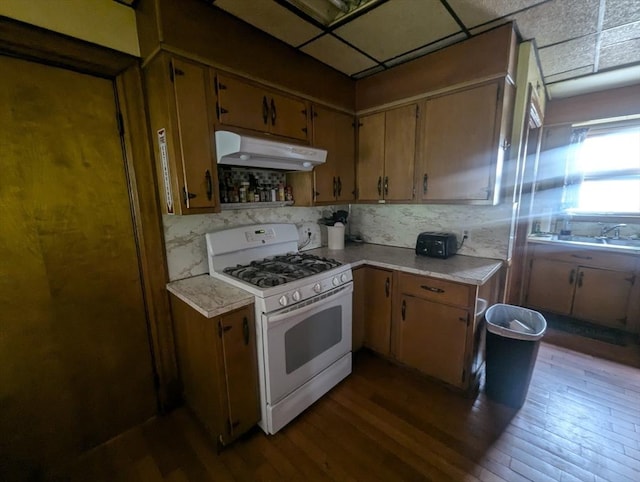 kitchen featuring dark wood-type flooring, white range with gas stovetop, under cabinet range hood, and light countertops