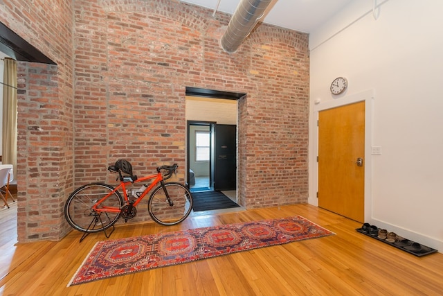 interior space featuring brick wall, baseboards, a high ceiling, and hardwood / wood-style floors