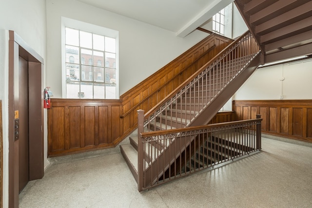 stairs featuring wood walls, wainscoting, and a healthy amount of sunlight