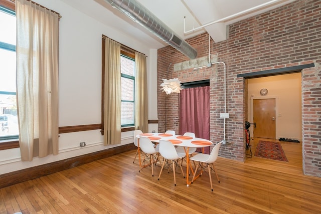 dining area with brick wall, baseboards, a high ceiling, and hardwood / wood-style floors