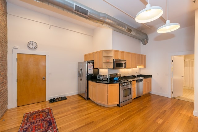 kitchen with a towering ceiling, open shelves, a sink, stainless steel appliances, and light wood-style flooring