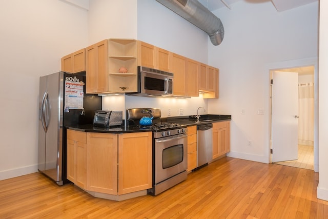 kitchen with light brown cabinets, a high ceiling, light wood-type flooring, a sink, and stainless steel appliances