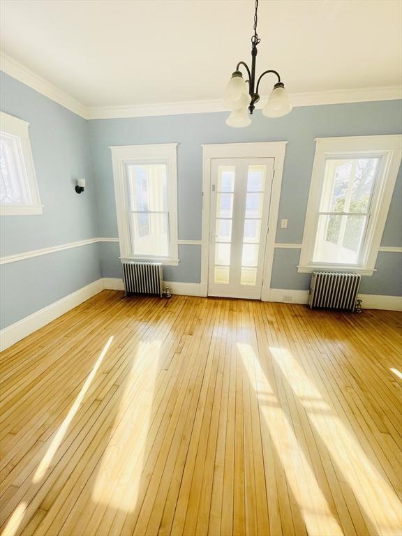 interior space featuring ornamental molding, radiator heating unit, an inviting chandelier, and light hardwood / wood-style flooring