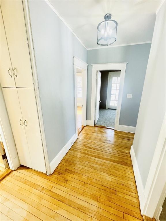 hallway featuring crown molding, a notable chandelier, and light hardwood / wood-style floors