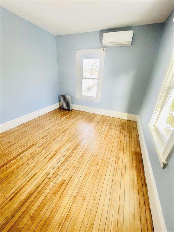 unfurnished room with radiator heating unit, a wall unit AC, and light hardwood / wood-style flooring