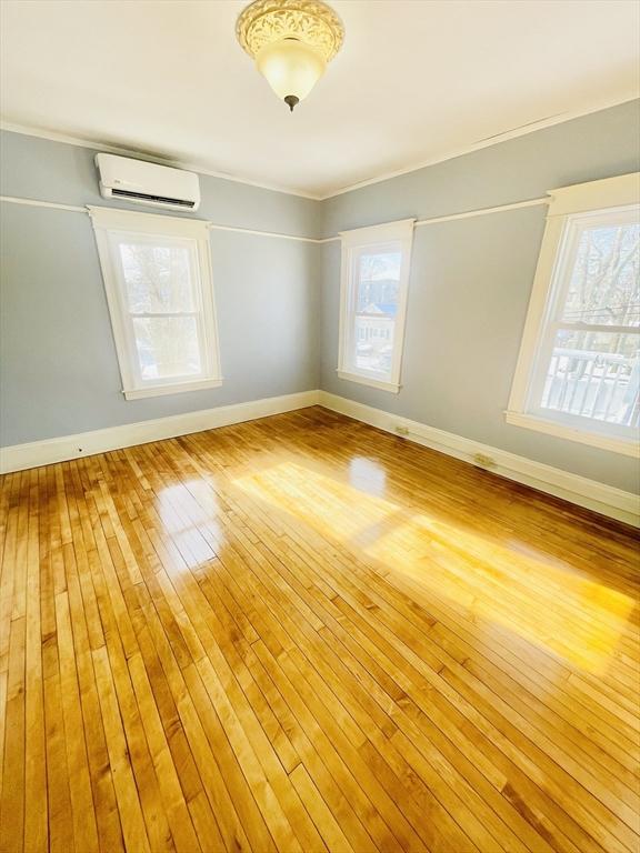 unfurnished room featuring a wealth of natural light, a wall unit AC, and light wood-type flooring