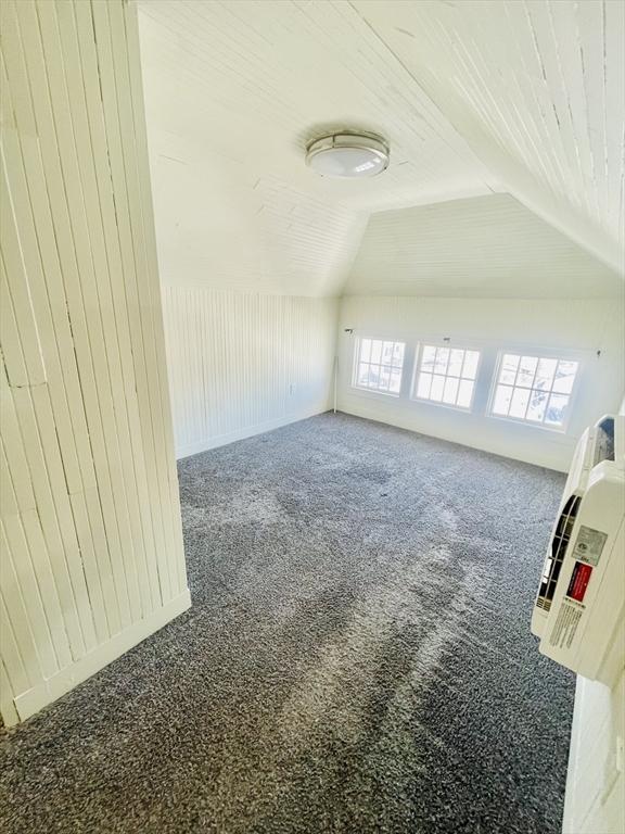 additional living space with vaulted ceiling, wooden walls, and carpet flooring