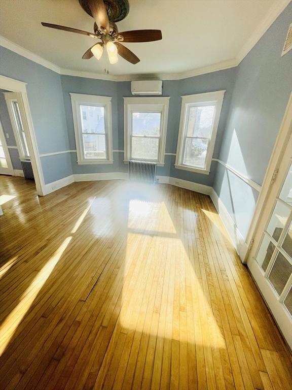 empty room with radiator heating unit, an AC wall unit, and light wood-type flooring