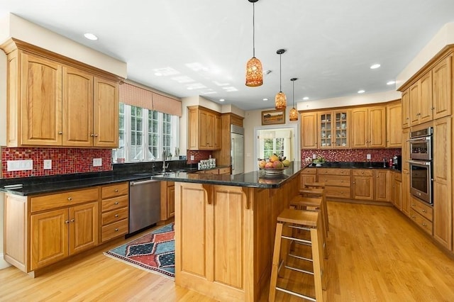 kitchen with a center island, a kitchen breakfast bar, light hardwood / wood-style flooring, pendant lighting, and appliances with stainless steel finishes