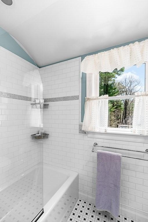 bathroom with tile patterned flooring, vaulted ceiling, a bathtub, and tile walls