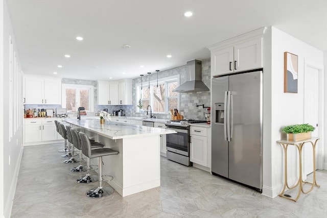 kitchen with wall chimney range hood, a breakfast bar area, stainless steel appliances, white cabinets, and a kitchen island