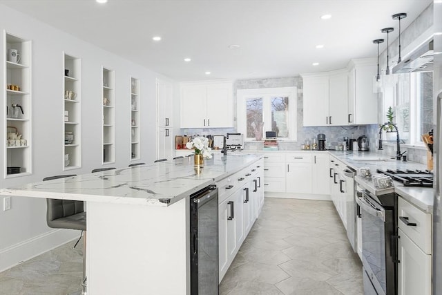 kitchen with sink, stainless steel gas range, white cabinetry, a spacious island, and beverage cooler