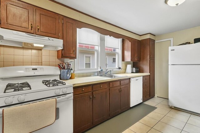kitchen featuring a sink, backsplash, under cabinet range hood, and white appliances