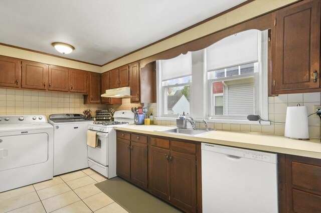 kitchen with white appliances, under cabinet range hood, washing machine and clothes dryer, a sink, and backsplash