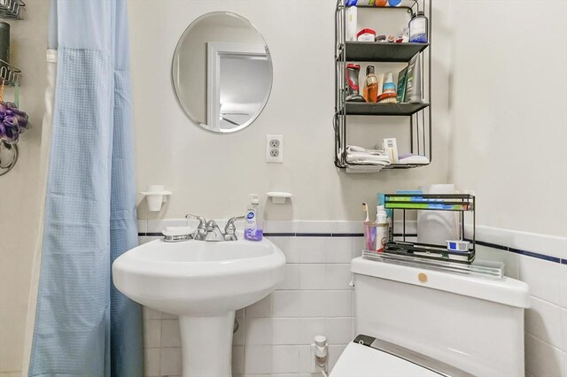 full bathroom featuring toilet, tile walls, and wainscoting