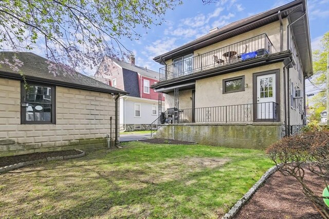 back of property with a yard, covered porch, a balcony, and stucco siding