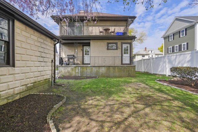 back of house with a porch, a lawn, fence, a balcony, and stucco siding