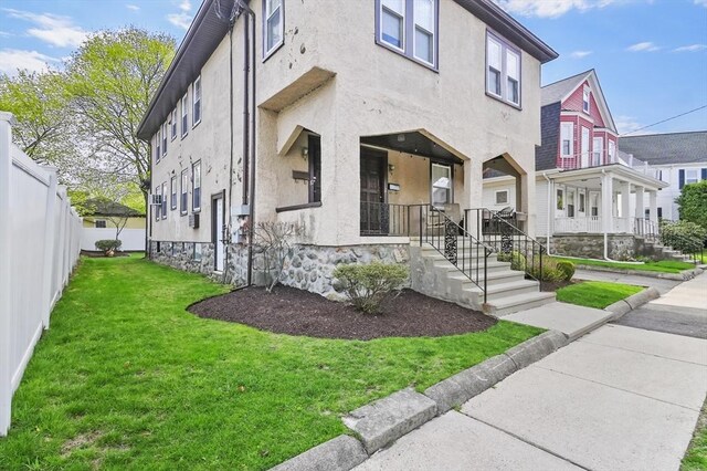exterior space with a porch, a residential view, fence, a front lawn, and stucco siding