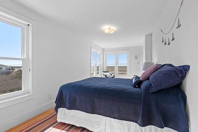 bedroom with multiple windows, baseboards, and wood finished floors