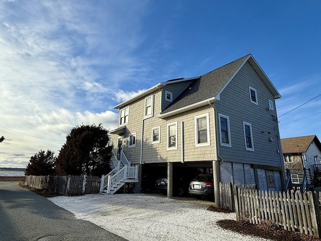 view of home's exterior with a carport, roof with shingles, gravel driveway, and a fenced front yard