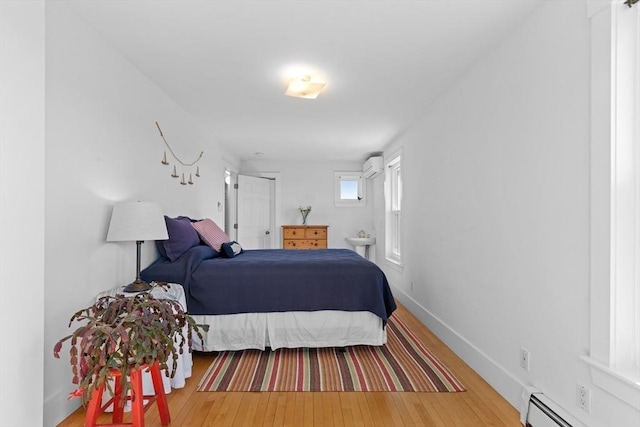 bedroom with a baseboard heating unit, wood-type flooring, an AC wall unit, and baseboards