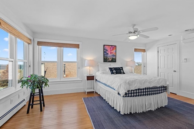 bedroom featuring wood-type flooring, baseboards, baseboard heating, and an AC wall unit