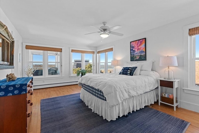 bedroom featuring ceiling fan, multiple windows, a baseboard radiator, and wood finished floors