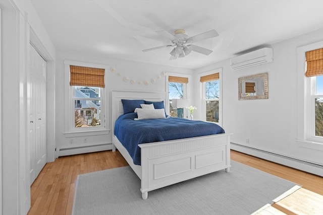 bedroom with a baseboard heating unit, a wall unit AC, light wood-style flooring, and a ceiling fan