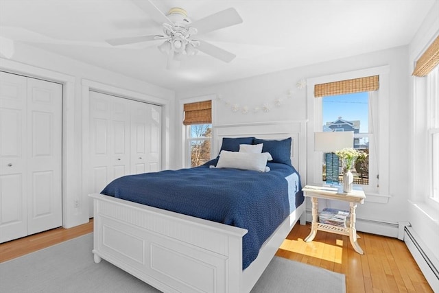 bedroom with light wood-style floors, a ceiling fan, baseboard heating, and two closets