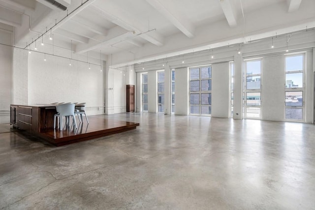 unfurnished living room featuring track lighting, beam ceiling, concrete floors, and a towering ceiling