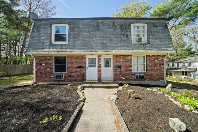 view of front facade featuring brick siding, mansard roof, fence, and roof with shingles