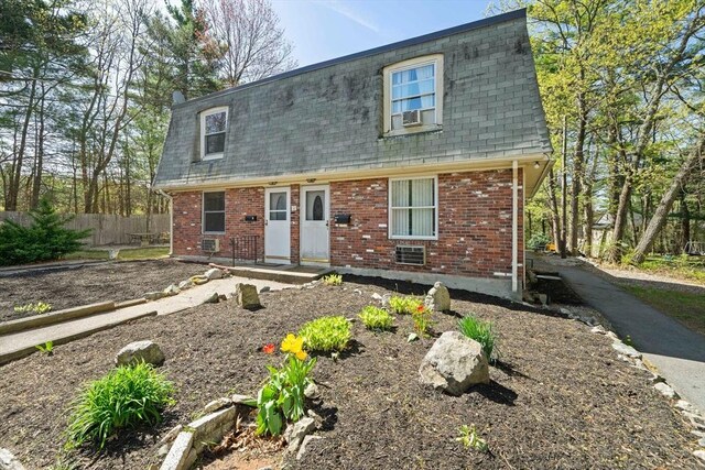 view of front of house featuring fence, a shingled roof, mansard roof, and brick siding