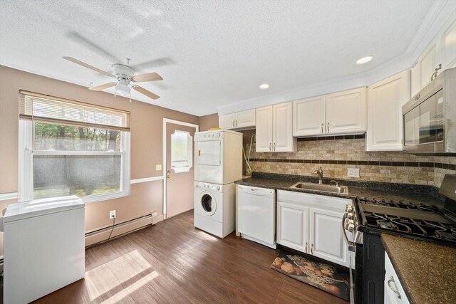 kitchen featuring dark countertops, a sink, stacked washing maching and dryer, stainless steel appliances, and a baseboard heating unit