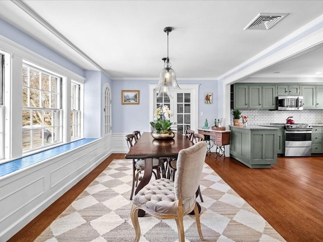 dining space featuring ornamental molding, wainscoting, visible vents, and light wood-style floors