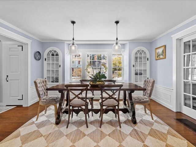 dining room featuring light wood finished floors, visible vents, crown molding, and wainscoting