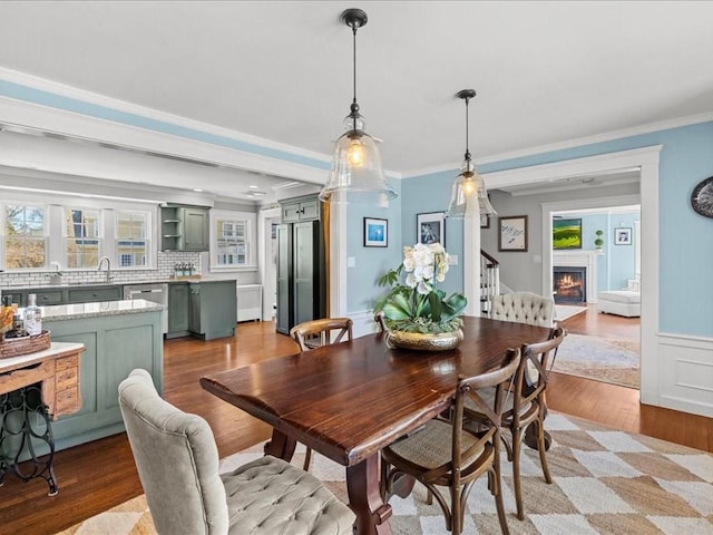 dining space featuring ornamental molding, light wood-type flooring, a warm lit fireplace, and stairway