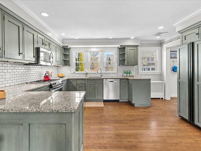 kitchen featuring light stone counters, crown molding, open shelves, appliances with stainless steel finishes, and a sink