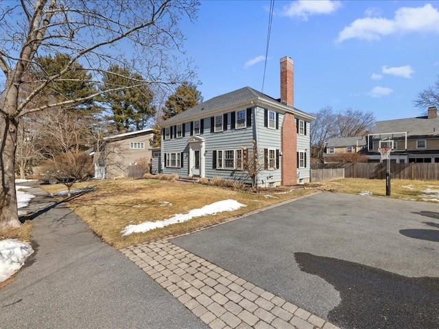 colonial house featuring aphalt driveway, entry steps, fence, and a chimney