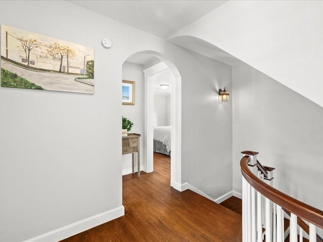 corridor with dark wood-style floors, arched walkways, and baseboards