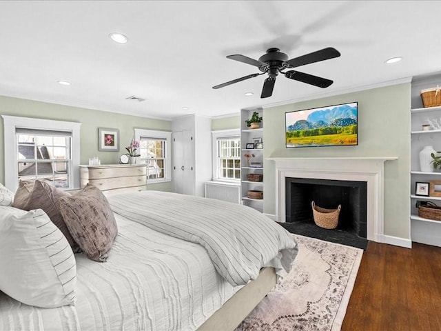 bedroom with dark wood-style flooring, recessed lighting, visible vents, ornamental molding, and a fireplace with flush hearth