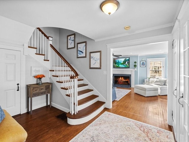 stairs with a fireplace with flush hearth, crown molding, baseboards, and wood finished floors