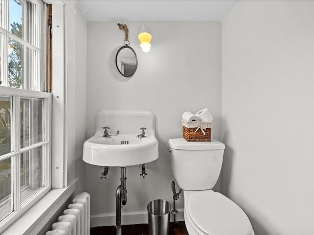 bathroom featuring radiator, baseboards, toilet, and a sink