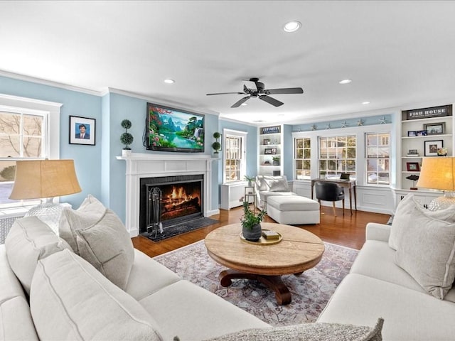 living area with a fireplace with flush hearth, built in shelves, wood finished floors, and crown molding