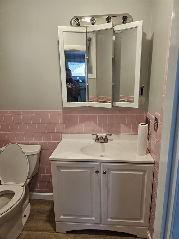 half bath featuring toilet, vanity, wainscoting, wood finished floors, and tile walls