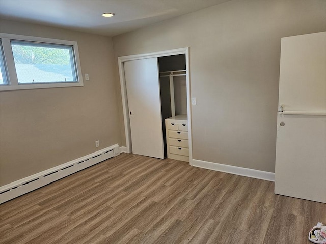 unfurnished bedroom featuring a closet, wood finished floors, baseboards, and a baseboard radiator