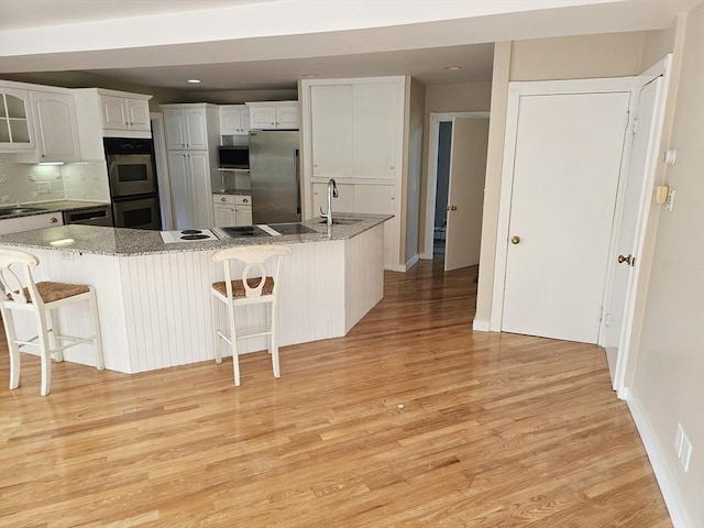 kitchen featuring a sink, light wood-style floors, appliances with stainless steel finishes, and a breakfast bar area