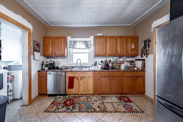 kitchen featuring appliances with stainless steel finishes, dark stone counters, sink, light tile patterned floors, and washing machine and clothes dryer